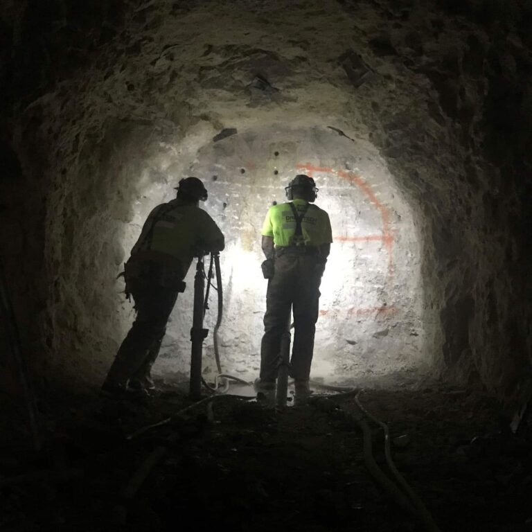 Miners drilling holes in rock prior to placing explosives